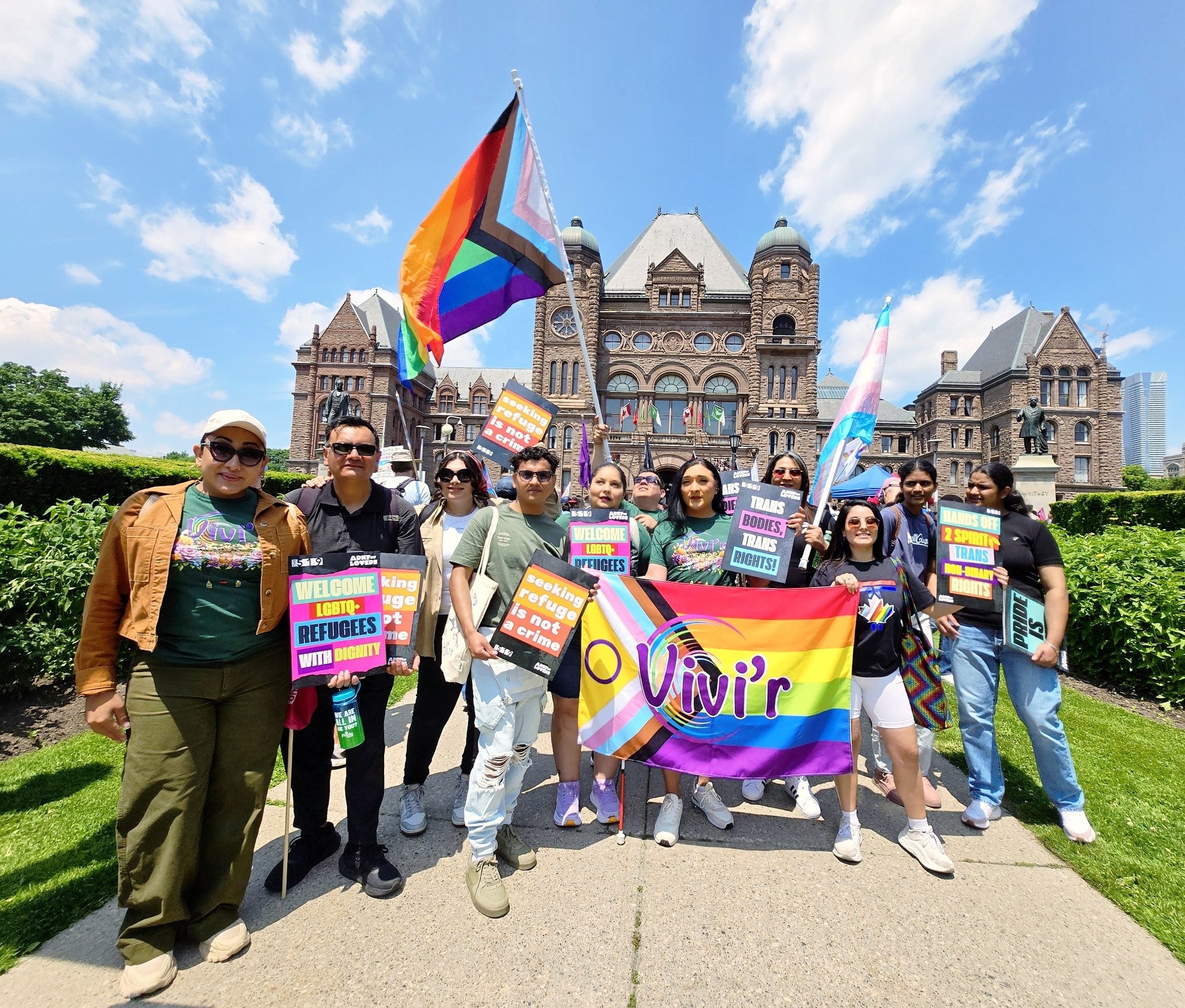 Community members at Queen's Park holding 'Welcome Trans Refugees With Dignity' signs